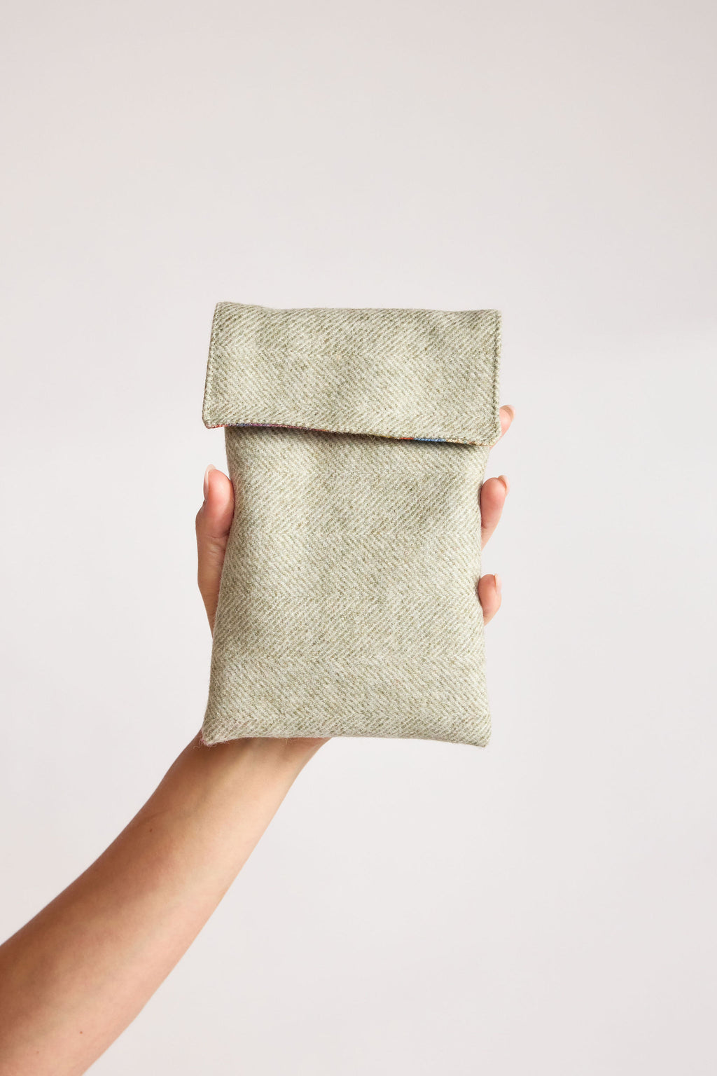 Mint green herringbone tweed phone pouch with printed lining, held in hand