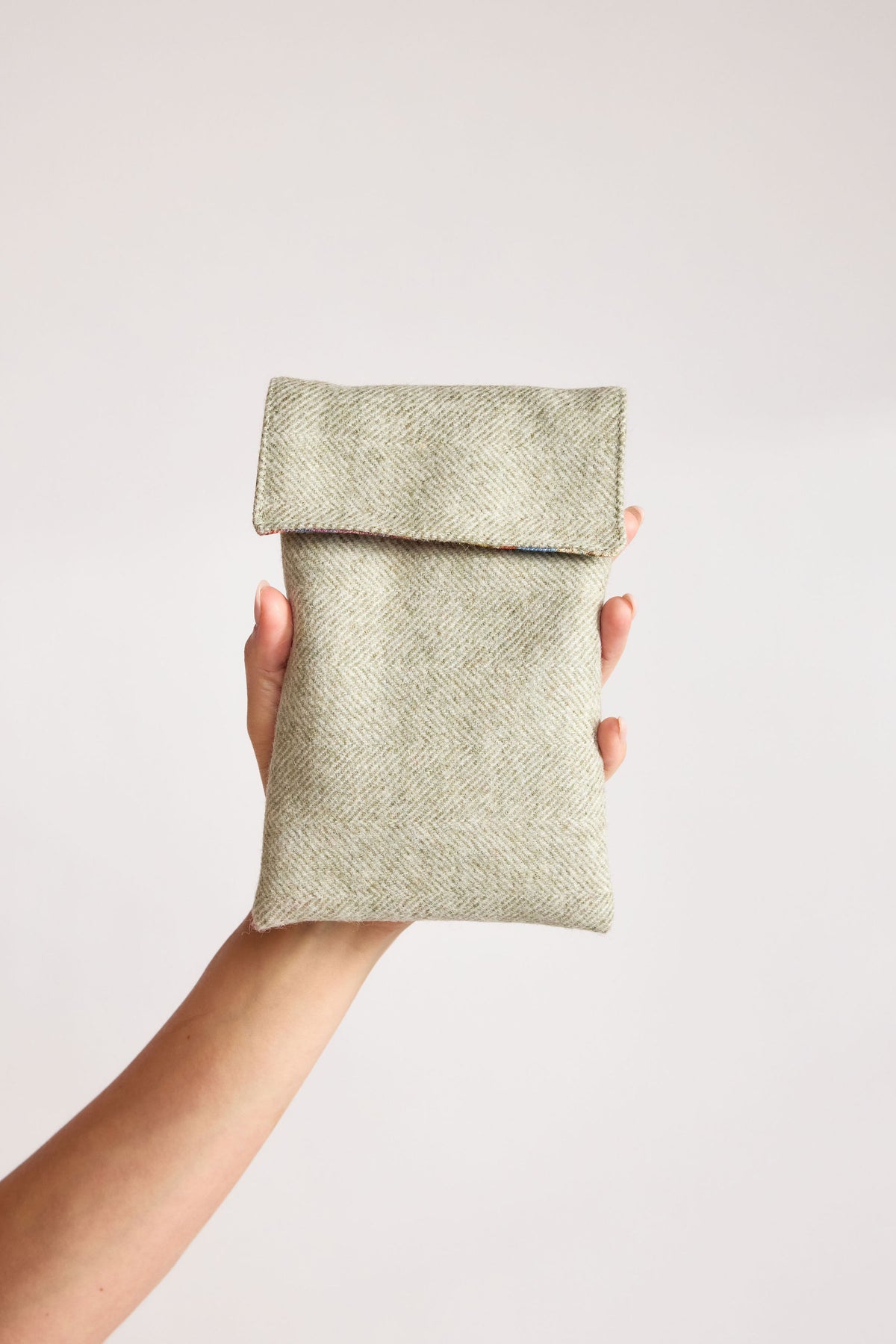 Mint green herringbone tweed phone pouch with printed lining, held in hand